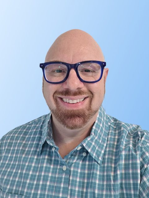 Brian Young smiling, in blue glasses and a teal plaid shirt, on a light blue background