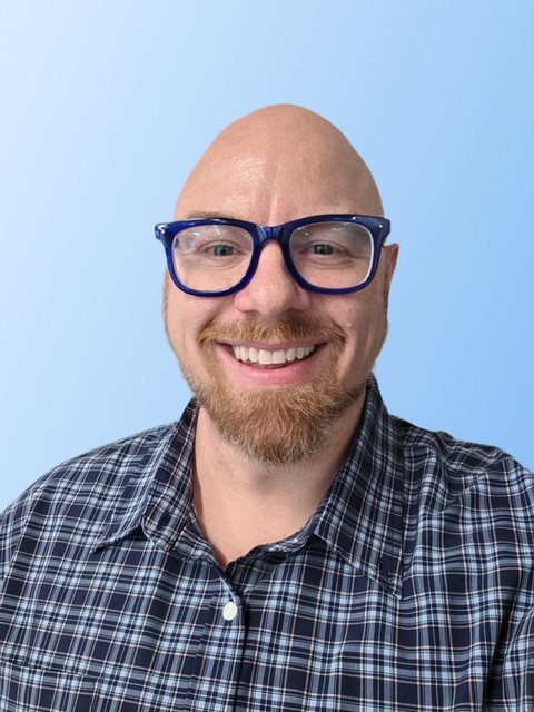 Brian Young smiling, in blue glasses and a navy plaid shirt, on a light blue background
